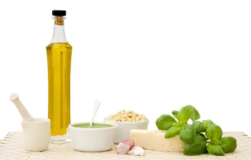 A bottle of olive oil, bowl of pesto and bowls of garlic.